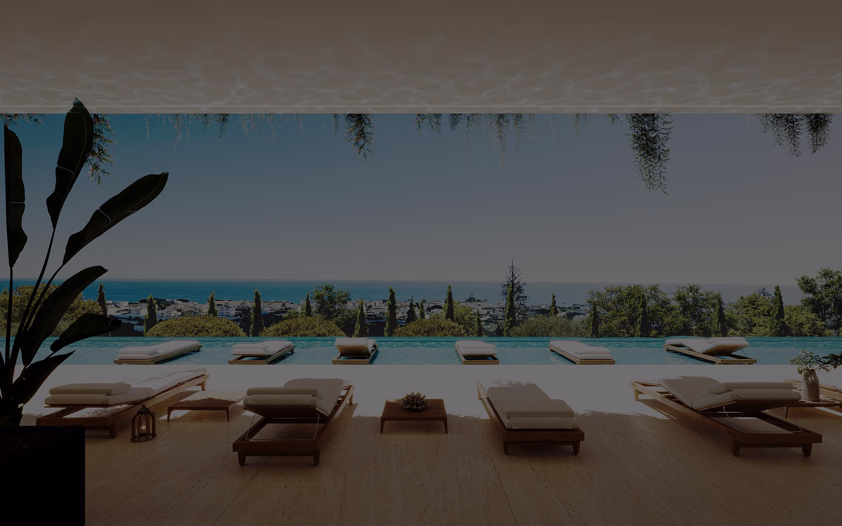 Luxury terrace overlooking the ocean, featuring an infinity pool surrounded by sun loungers and lush greenery. The horizon blends the sky and sea, creating a serene and inviting atmosphere.